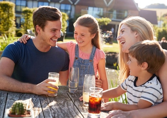 Mother, father, a young boy and young girl sat around a picnic table enjoying drinks in the sunshine