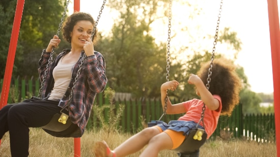 A mother and her daughter having fun in the park on swings