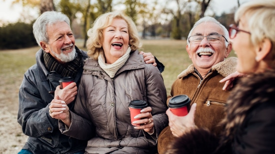 Older couples sat on a bench in the park drinking coffee