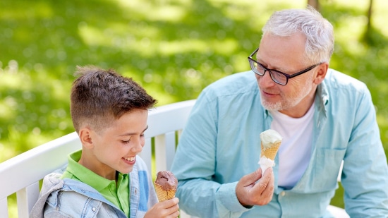 Older man enjoying ice cream on a park bench with a little boy