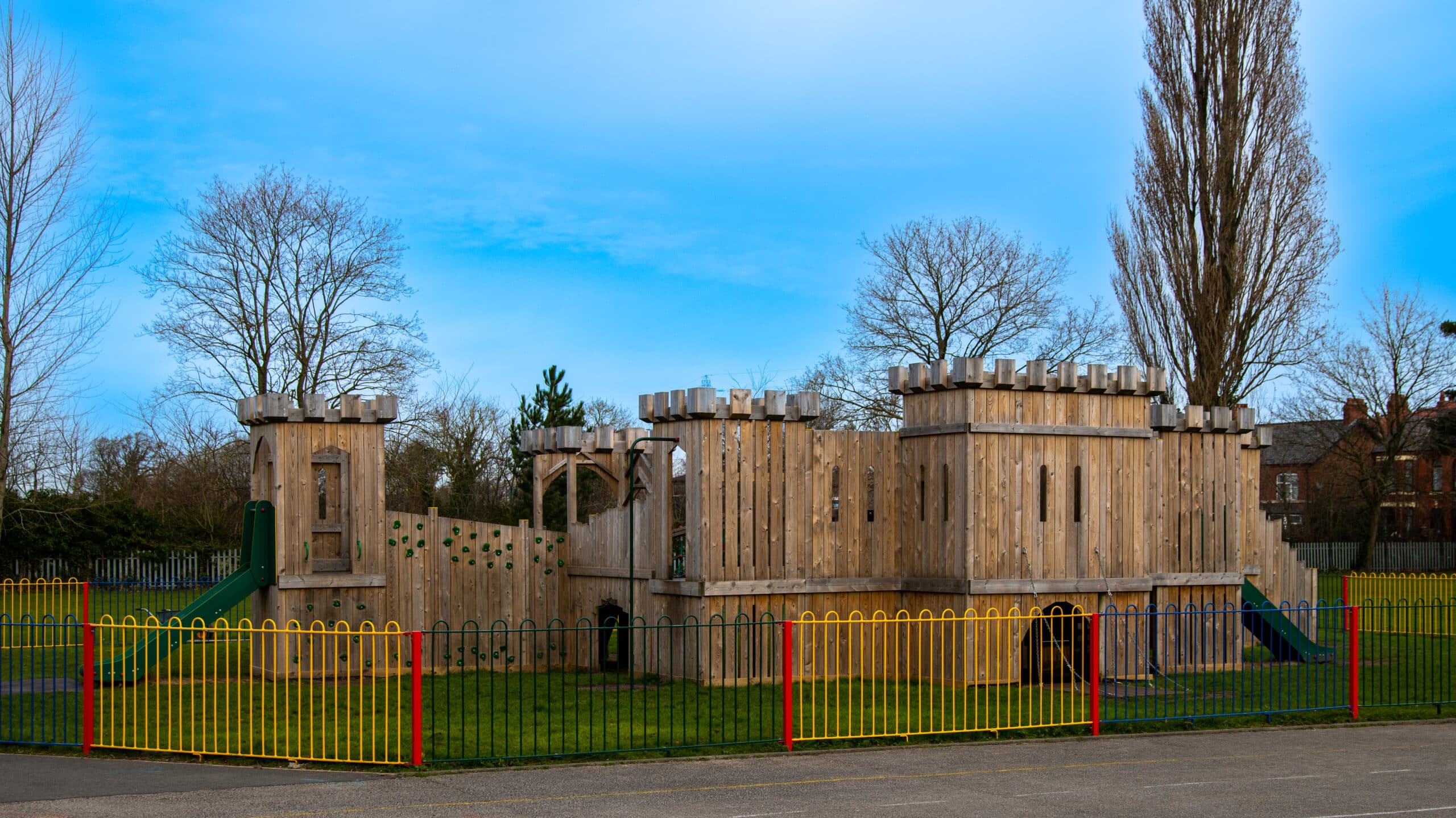 A wooden playground castle with a colourful metal fence in the foreground