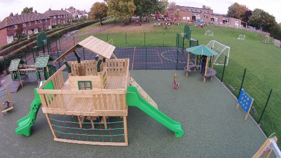 Outdoor play area featuring a wooden hut at the foreground and a ball game area in the background