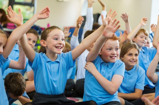 Children in blue uniforms eager to answer questions in class by raising their hands up