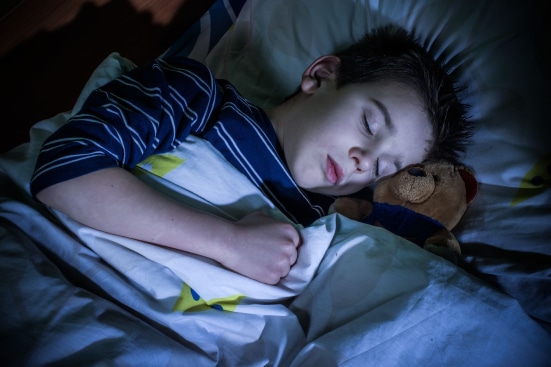 Boy clutching his teddy as he sleeps soundly in a dark room