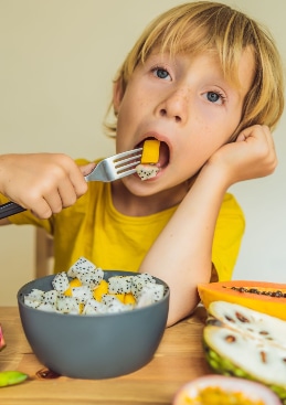 Boy in yellow top eating fruit from a bowl with a fork