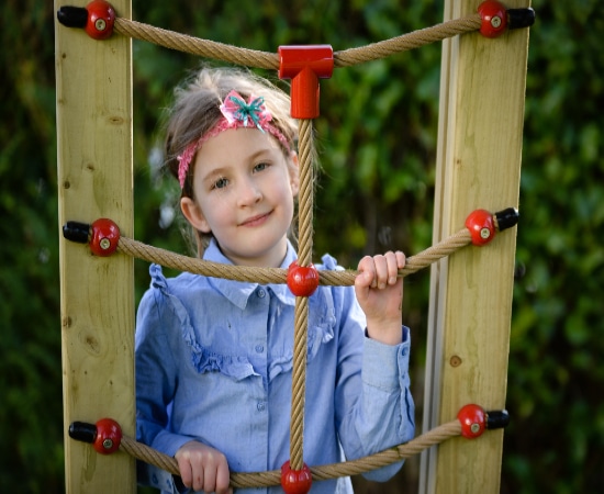 A little girl holds on to some ropes attached to timber in a playground