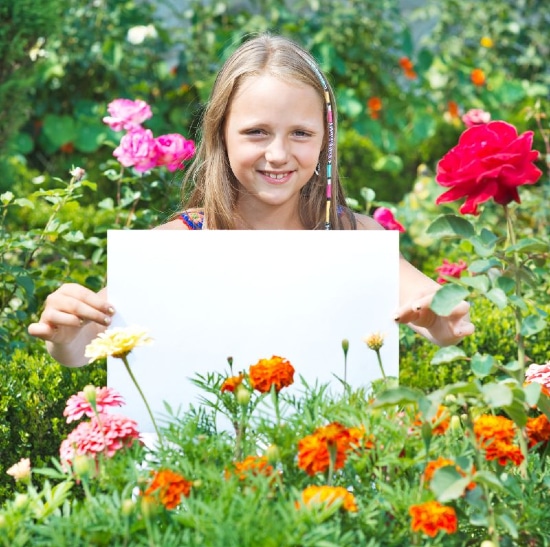 Girl surrounded by flowers holding a large blank canvas up for the camera