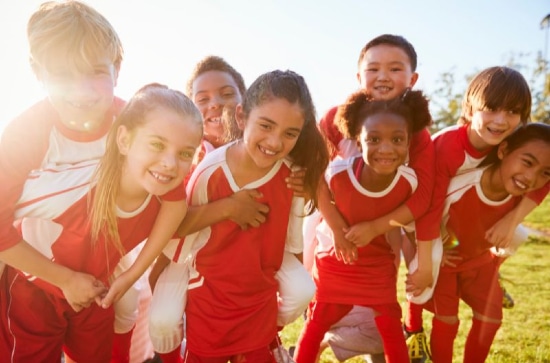 Several children dressed in red sports kits mugging the camera, looking happy