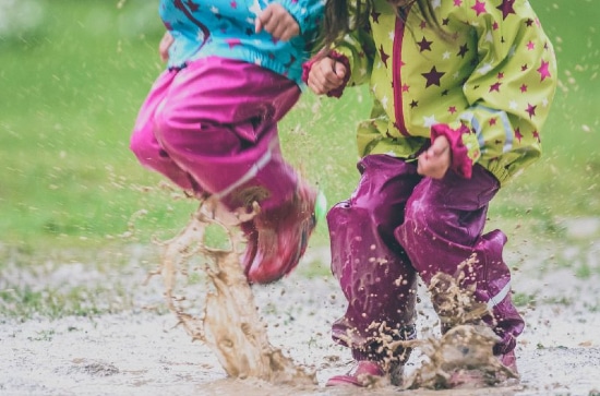 Two children wearing wellies jumping up and down in a muddy puddle