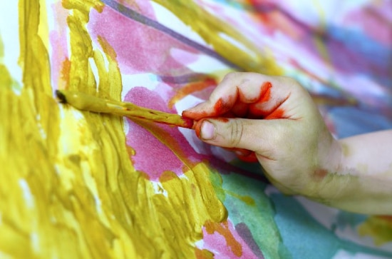 Close up of a child's hand painting yellow around pink hearts