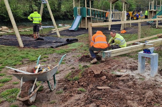 Men in high-vis jackets installing a playground in a muddy field