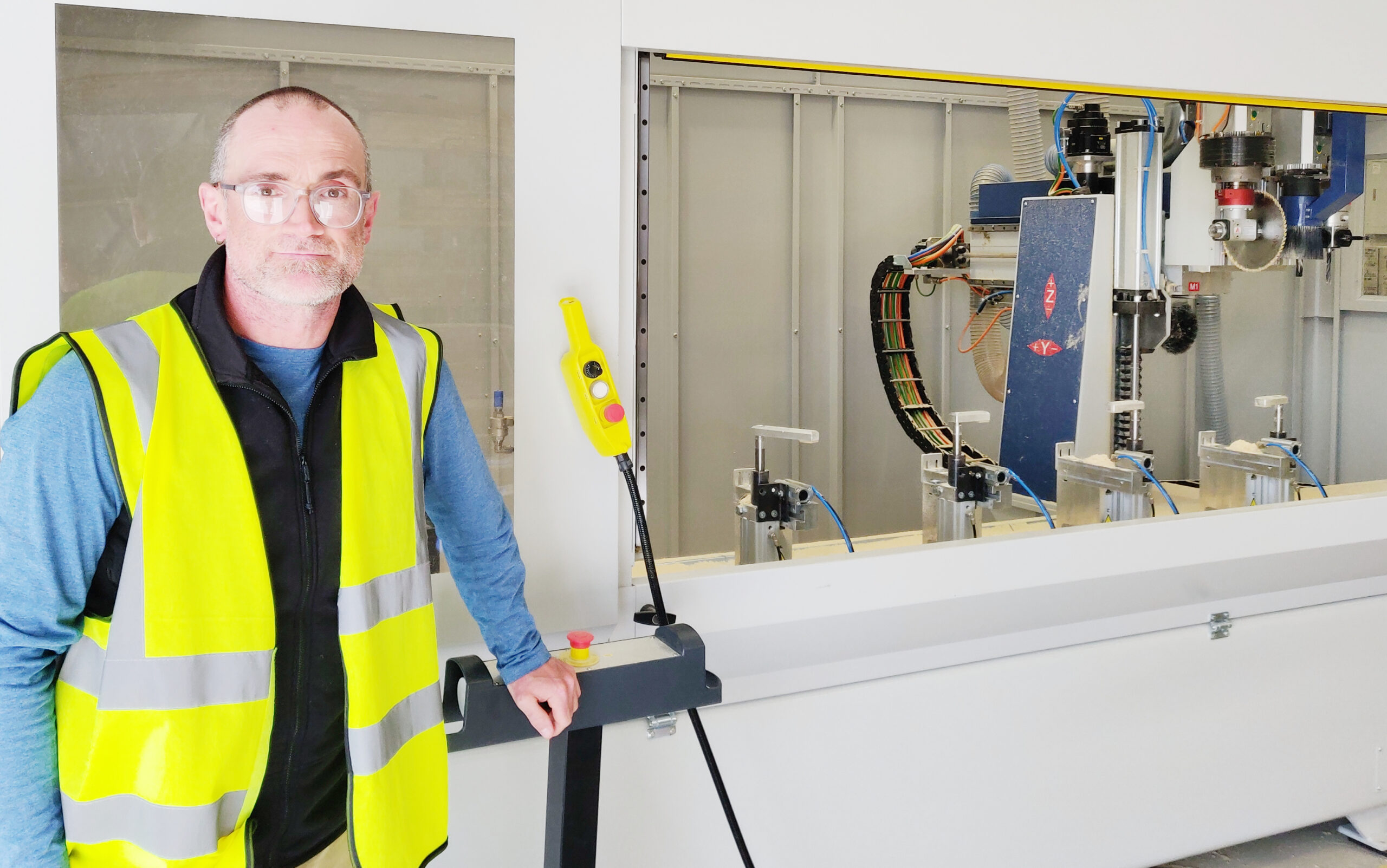 Mid shot of a man in high-vis vest posing in front of a high-tech woodwork machine