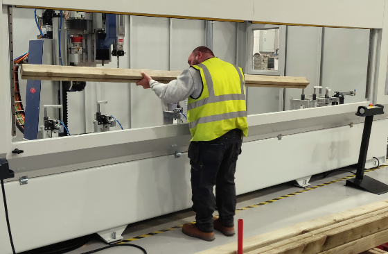 High-Vis vested man loading timber into a high-tech woodworking machine