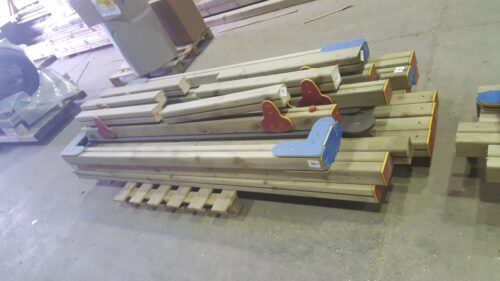 A stack of playground equipment components, all made of wood with recycled plastic caps, sat on a factory floor