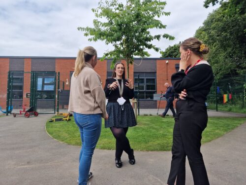 Three professional looking women chatting outside a school near a tree and some grass