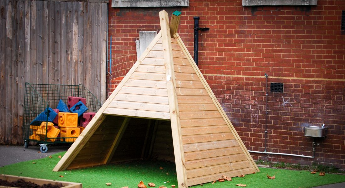 timber teepee playhouse on artificial grass in a school playground