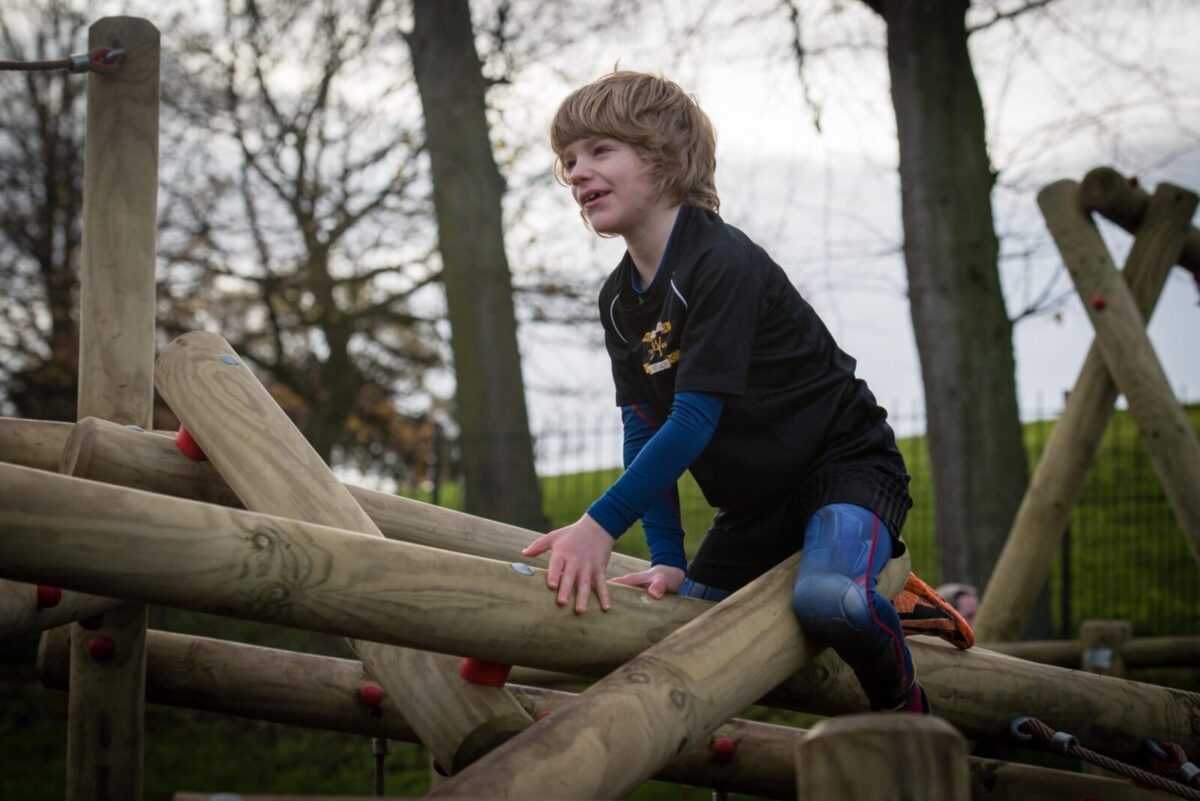 Boy On Round Timber Jungle Climbing Frame