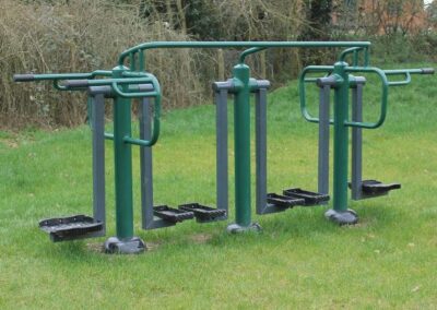 Three green metal permanently installed exercise items on grass