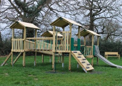 Four tower wooden play structure featuring a slide set on grass