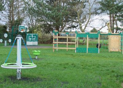 Wooden climbing structure in the background, metal spinning equipment in the foreground at a children's grass park