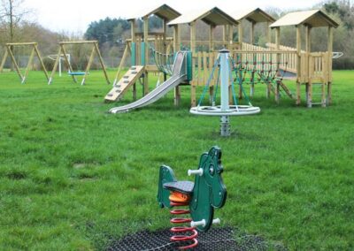Wooden play towers in the background, green dragon springer play seat in the foreground in a grass field