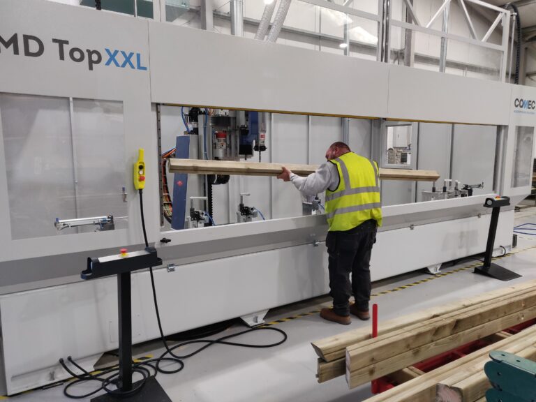 Man in high-vis loading timber into a large grey cutting and drilling machine