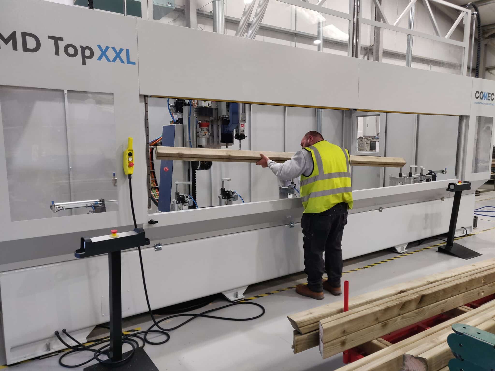 Man in high-vis loading timber into a large grey cutting and drilling machine