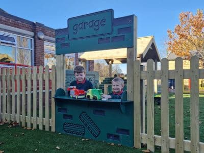 two boys in school uniform play at a garage themed play panel