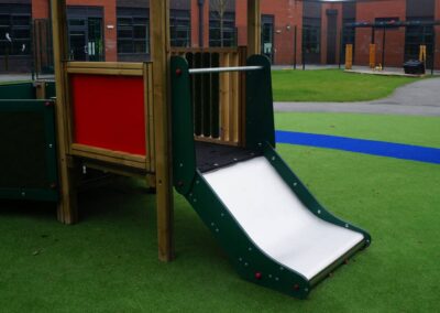 Side view of a metal slide which is part of a timber play tower structure at a grassy play area