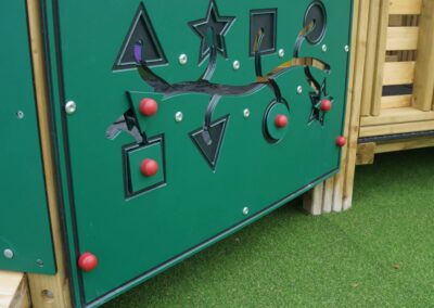 Green play panel featuring shapes attached to a wooden play tower