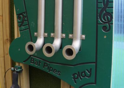 Three batpipes forming part of a green musical play panel instrument at a playground