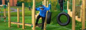 Child holding on to a tyre swing while navigating a chain bridge