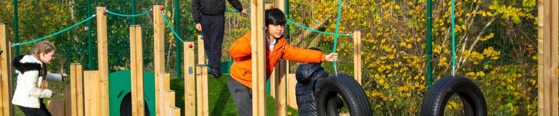 boy in orange coat playing on timber outdoor play equipment