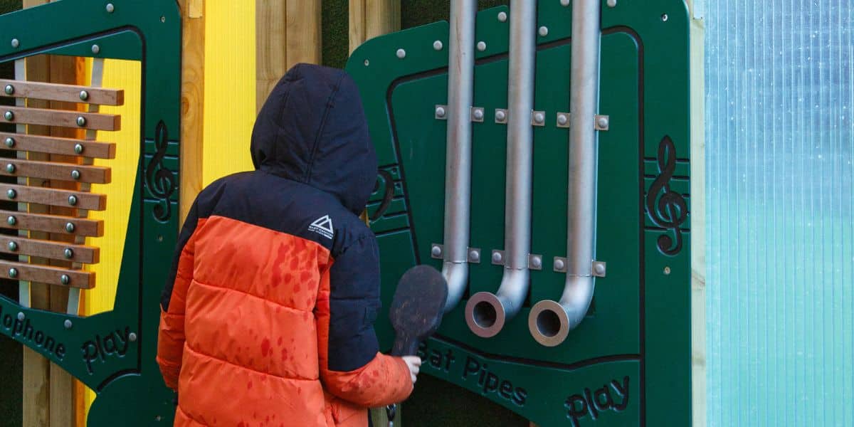 This image shows a male student playing with the bat pipes playground equipment