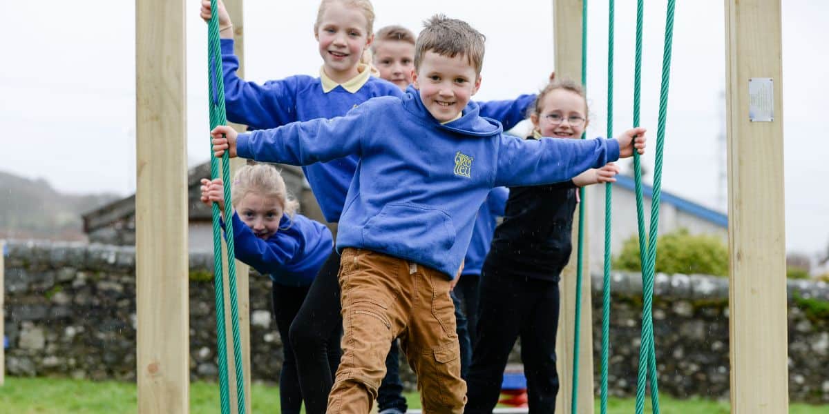 In this image it shows children playing on a rope bridge in their local community park