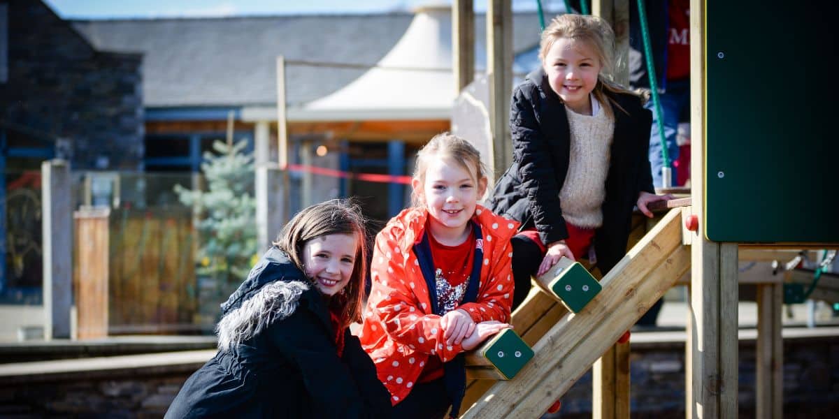 In this image it shows children playing on a wooded playtower in their local community park