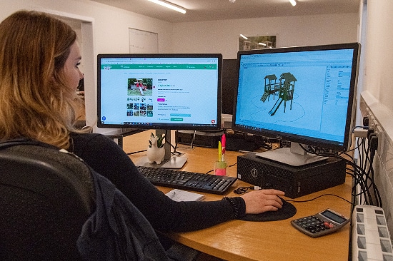 Woman uses a computer with two monitors to design playground equipment