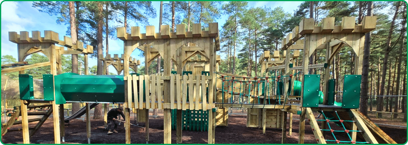 The back of a large timber play tower structure in the woods, featuring climbing elements for children