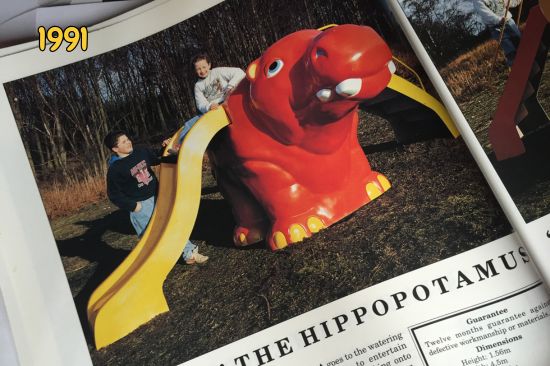 This image shows a play area in the early 1990s with a red plastic hippowith a built in yellow slide with two children playing on the playground equipment