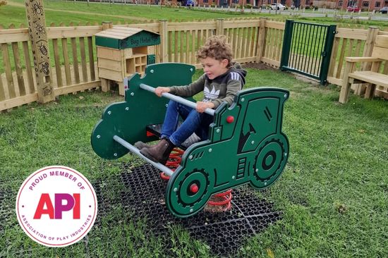 This image shows a young boy playing in a tractor spring rider piece of playground equipment with the Application Programming Interface (API) logo in the left hand corner