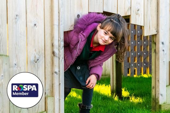 A girl in purple coat peeking out from within a timber castle with the RoSPA logo to her left