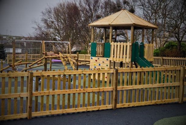 Vignette of timber play tower surrounded by timber fencing in a wet pour surfaced playground