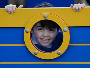 boy peering through porthole on blue timber play ship
