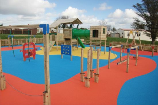 Colourful Caravan Park timber play towers and other play equipment on blue and red wet pour surfacing with caravans in the background