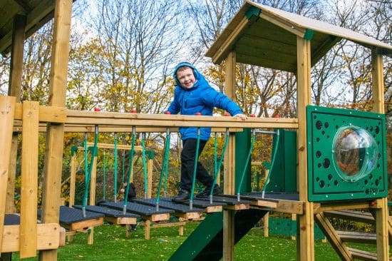 New Website Imagery - 2026 - New Website Imagery Playground Design Resource (4) This image shows a young male pupil waring ear defenders walking across a rope wooden bridge