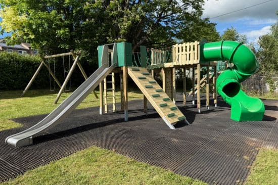 This image shows a playground that has a play tower installed on grass mats