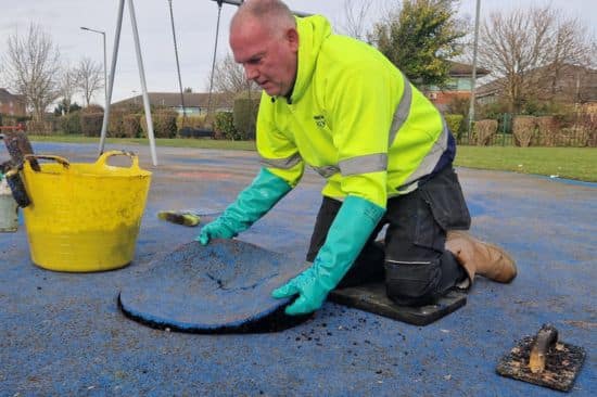 This image shows a male project manager conducting a wet pour repair on a playground surface