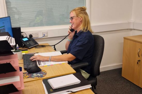 This image shows a female office worker taking phone calls whilst working on a desktop pc