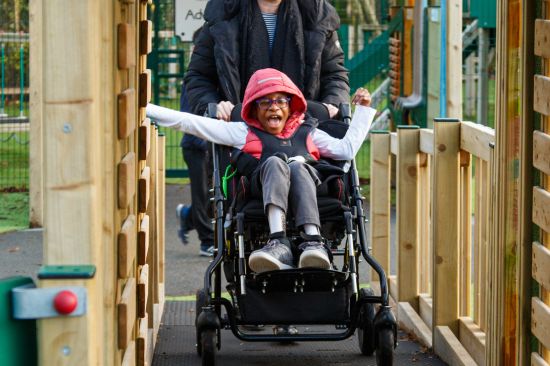 This image shows a young black girl in a wheel chair being pushed up a ramp by her teacher