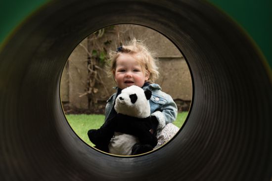 New Website Imagery - EYFS (6) This image shows a young female toddler in a mound tunnel holding a panda bear cuddly toy